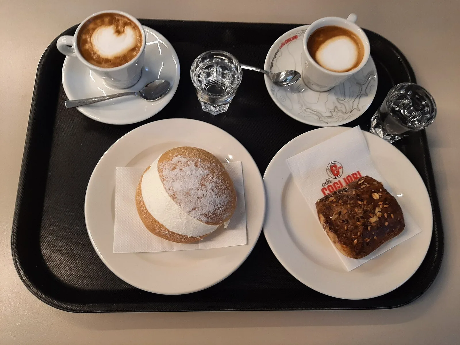 Un vassoio da colazione con due cappuccini, un maritozzo e un dolce da forno
